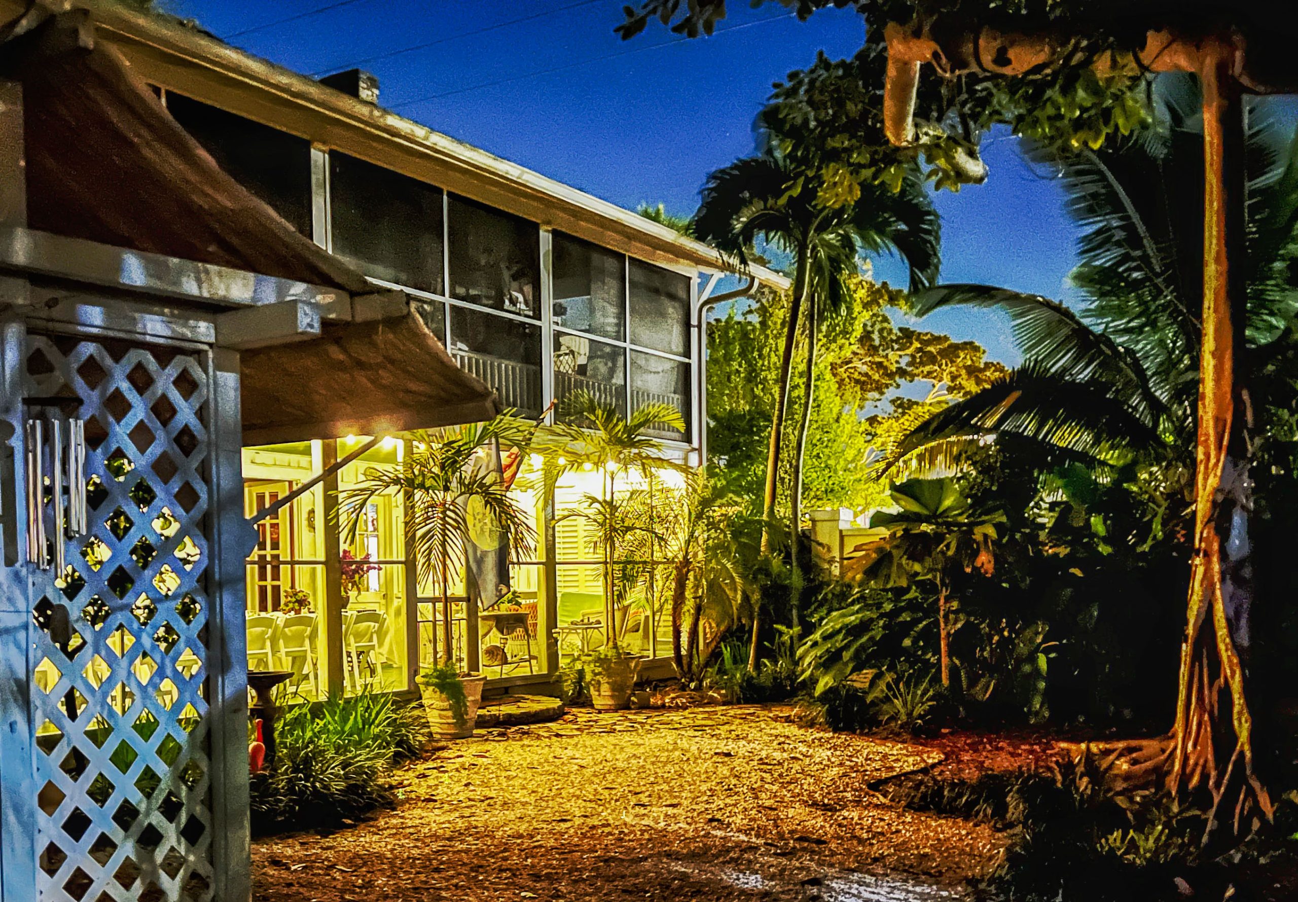 Warmly lit Arsenault cottage and tropical garden at dusk